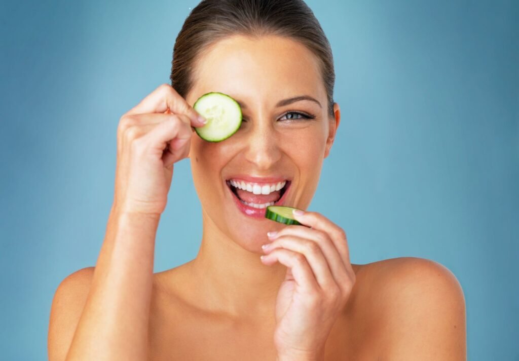mulher com pele saudável mordendo uma rodela de pepino e com outra no olho