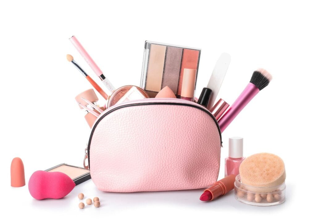 maleta de maquiagem na cor rosa, com diversos itens de maquiagem dentro e sobre a mesa