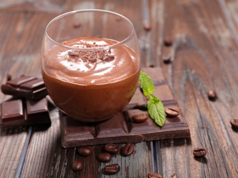 taça com mousse de chocolate sobre uma barra de chocolate em uma mesa marrão com grãos secos espalhados pela mesa