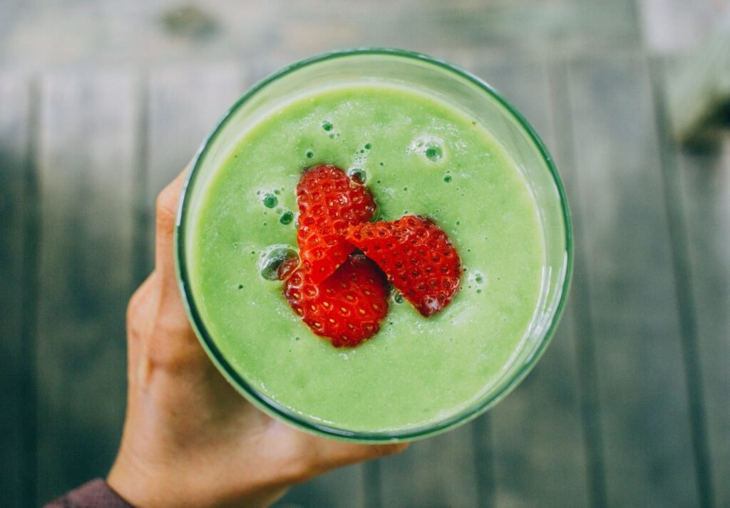 imagem de um copo de smoothie verde com morangos em cima