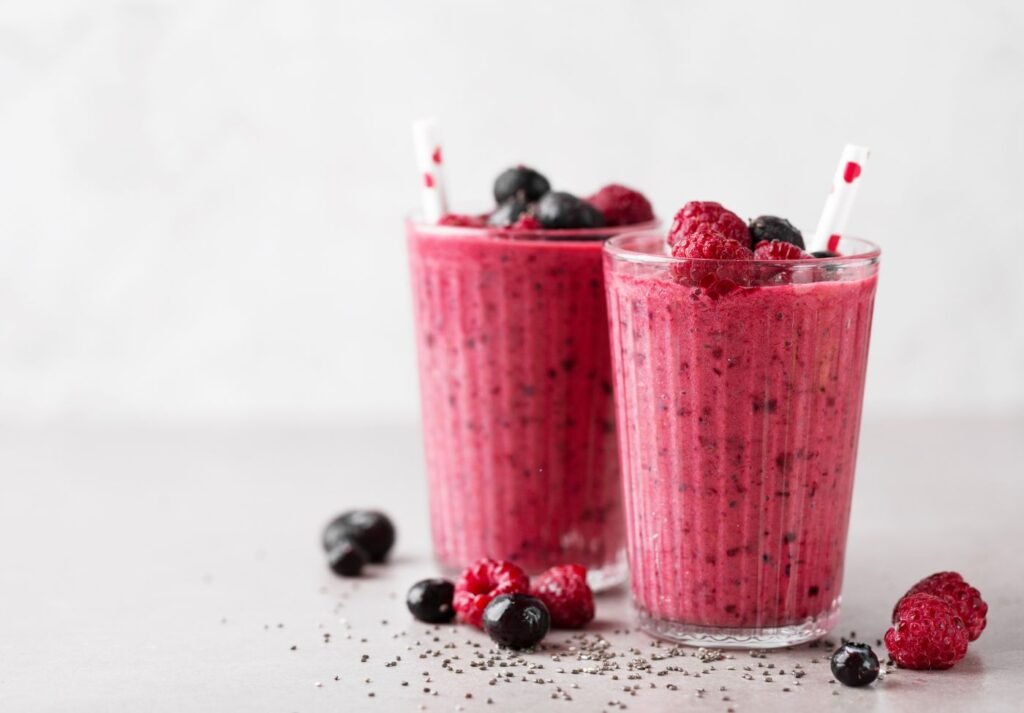 dois copos cheios de smoothie energizante, o liquido é vermelho com morangos e framboesa sobre a mesa