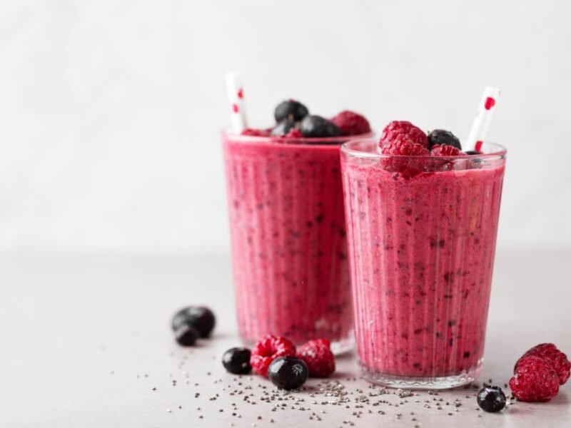 dois copos cheios de smoothie energizante, o liquido é vermelho com morangos e framboesa sobre a mesa
